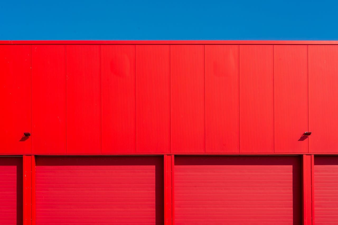 Bright red garage doors of an industrial building against a clear blue sky, showcasing minimalism.